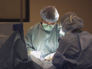 Surgeon making incision during surgery with scrub nurse assisting.